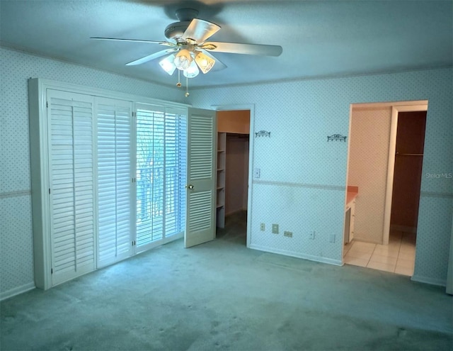 unfurnished bedroom with a walk in closet, ceiling fan, and light colored carpet