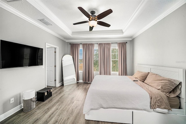 bedroom featuring hardwood / wood-style flooring, ceiling fan, crown molding, and a tray ceiling