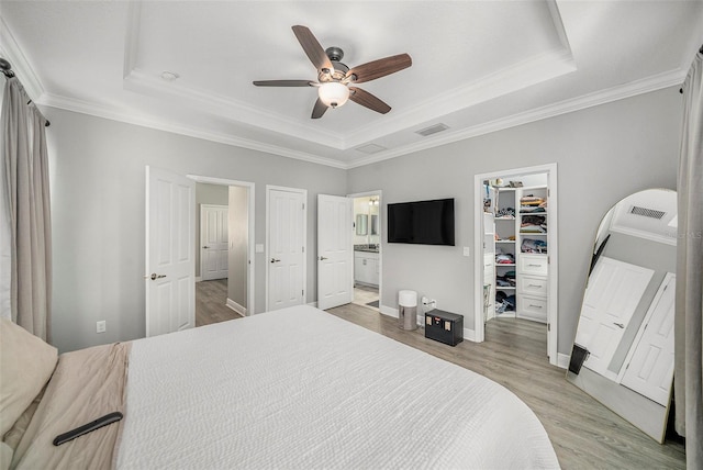 bedroom with ensuite bath, light hardwood / wood-style flooring, ceiling fan, a spacious closet, and a tray ceiling