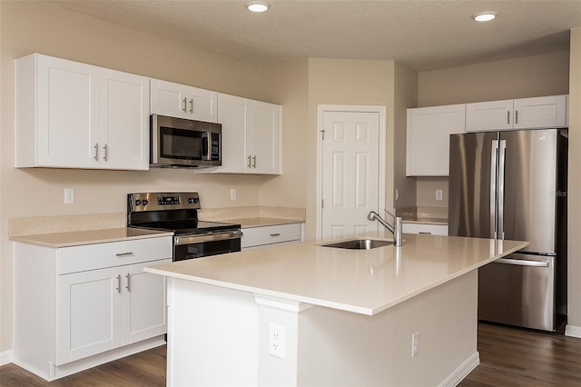 kitchen with sink, an island with sink, appliances with stainless steel finishes, dark hardwood / wood-style flooring, and white cabinetry