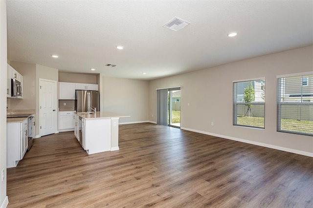 kitchen with hardwood / wood-style floors, appliances with stainless steel finishes, white cabinetry, and an island with sink