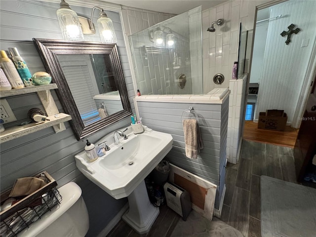 bathroom featuring sink, tiled shower, hardwood / wood-style flooring, toilet, and wood walls