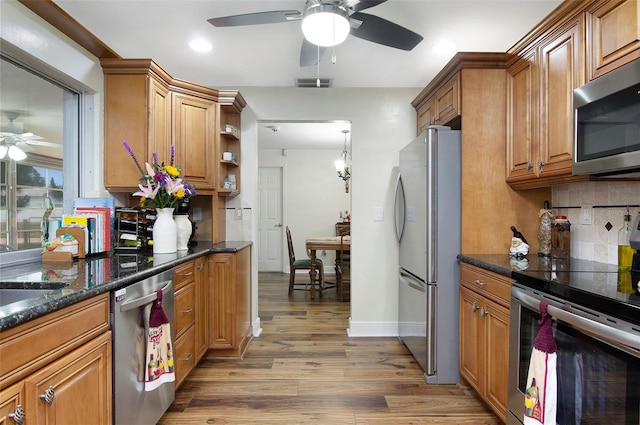 kitchen featuring backsplash, dark stone countertops, wood-type flooring, and appliances with stainless steel finishes