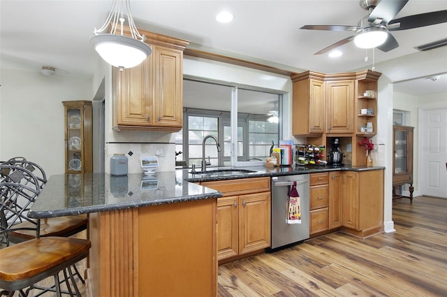 kitchen featuring stainless steel dishwasher, dark stone counters, a breakfast bar, sink, and light hardwood / wood-style flooring