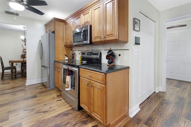 kitchen featuring dark hardwood / wood-style flooring, tasteful backsplash, stainless steel appliances, ceiling fan, and dark stone countertops