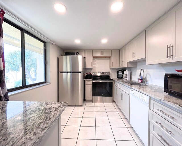 kitchen with sink, white cabinetry, stainless steel appliances, light stone countertops, and light tile patterned flooring