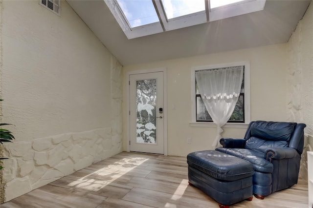 sitting room with visible vents, vaulted ceiling with skylight, a textured wall, and wood finished floors