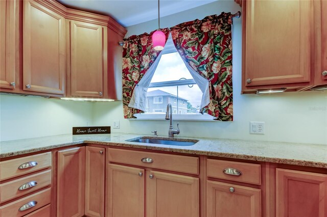 kitchen featuring a sink, decorative light fixtures, and light stone counters