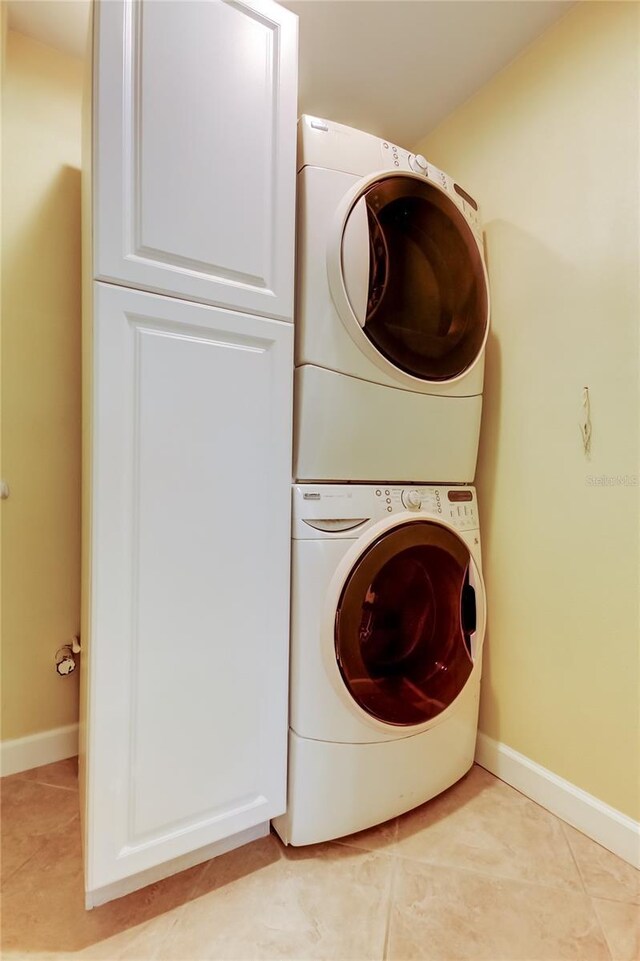 laundry room with light tile patterned flooring, cabinet space, baseboards, and stacked washer and dryer