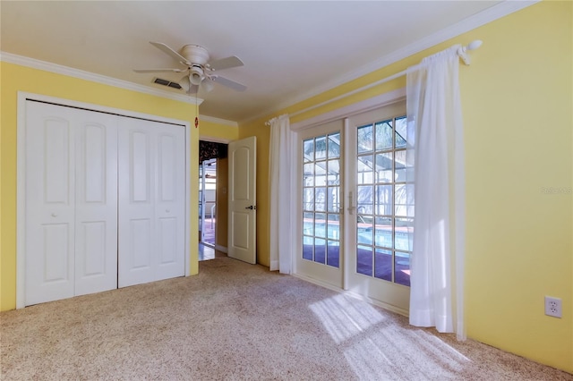 unfurnished bedroom featuring visible vents, a ceiling fan, a closet, carpet floors, and crown molding