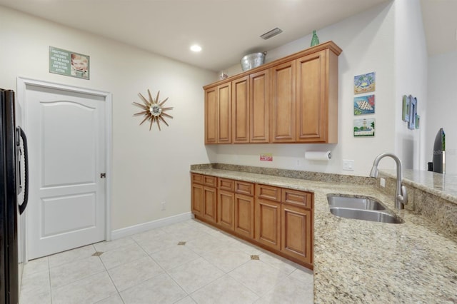 kitchen with black fridge, light stone counters, sink, and light tile patterned floors