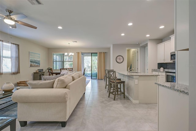 tiled living room with ceiling fan with notable chandelier