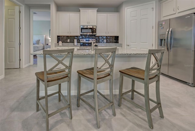 kitchen with a kitchen breakfast bar, stainless steel appliances, white cabinetry, and light stone counters