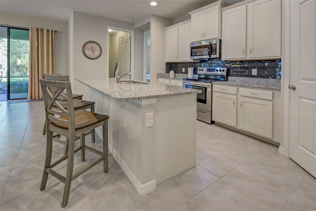 kitchen featuring backsplash, a kitchen island with sink, white cabinets, light stone countertops, and appliances with stainless steel finishes