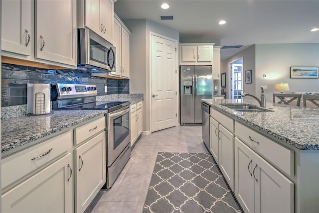 kitchen with a kitchen island with sink, sink, decorative backsplash, appliances with stainless steel finishes, and light stone counters