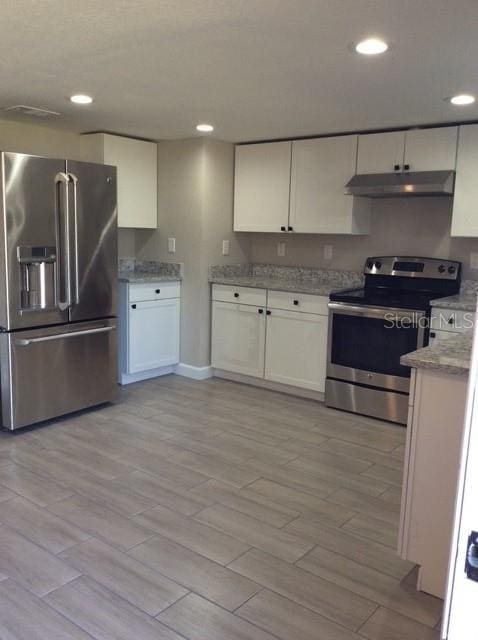 kitchen featuring light hardwood / wood-style floors, light stone counters, white cabinetry, and appliances with stainless steel finishes