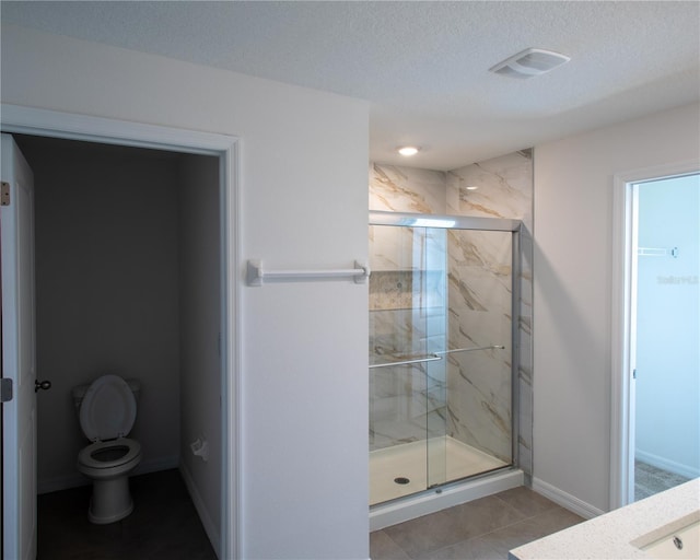 bathroom featuring an enclosed shower, vanity, a textured ceiling, tile patterned flooring, and toilet