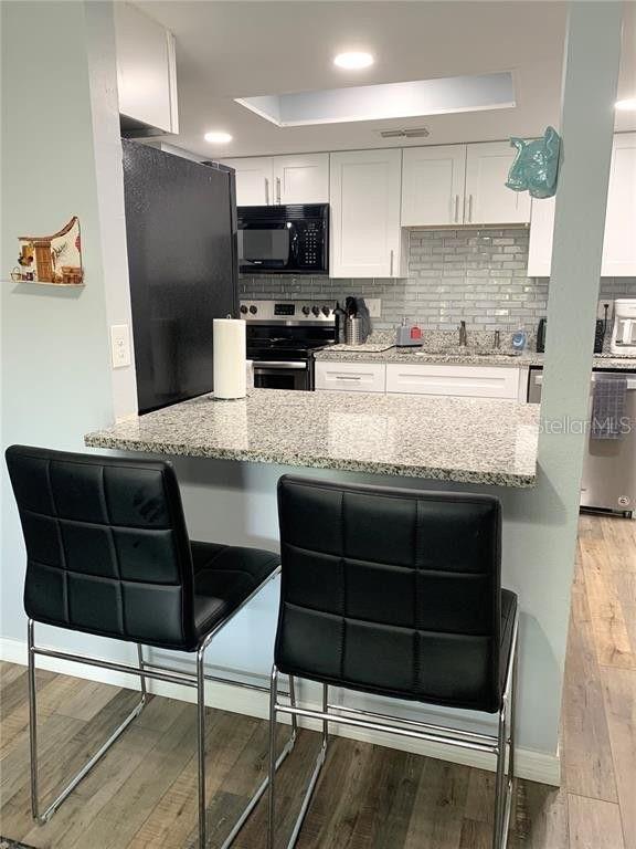 kitchen featuring light stone countertops, kitchen peninsula, black appliances, light hardwood / wood-style flooring, and white cabinetry