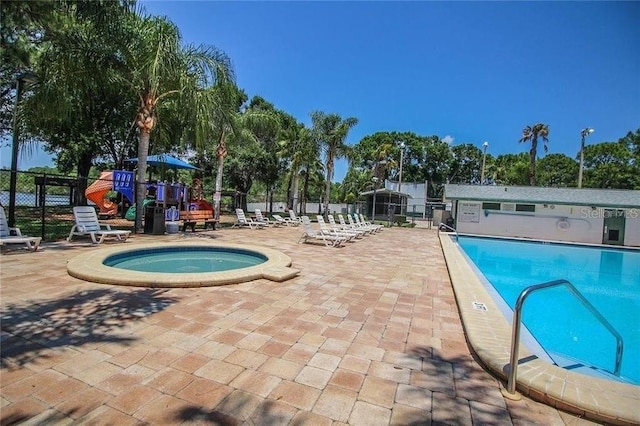 view of swimming pool with a playground, a patio, and a hot tub