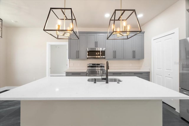 kitchen with decorative light fixtures, stainless steel appliances, gray cabinets, and a kitchen island with sink