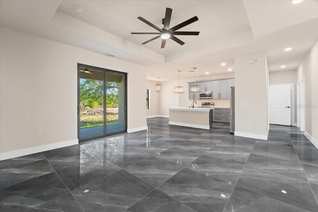 unfurnished living room featuring a raised ceiling, ceiling fan, and sink