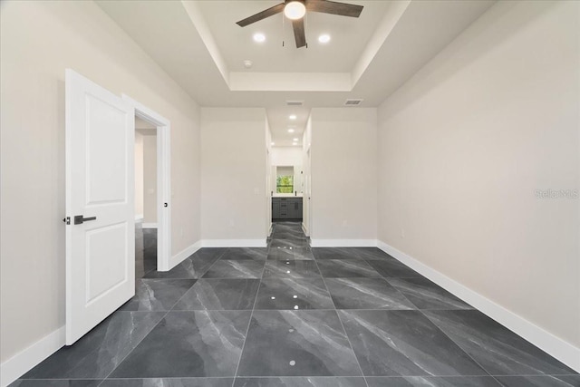 empty room with ceiling fan and a raised ceiling