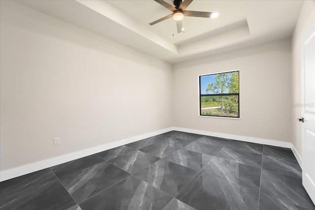 unfurnished room with ceiling fan and a tray ceiling