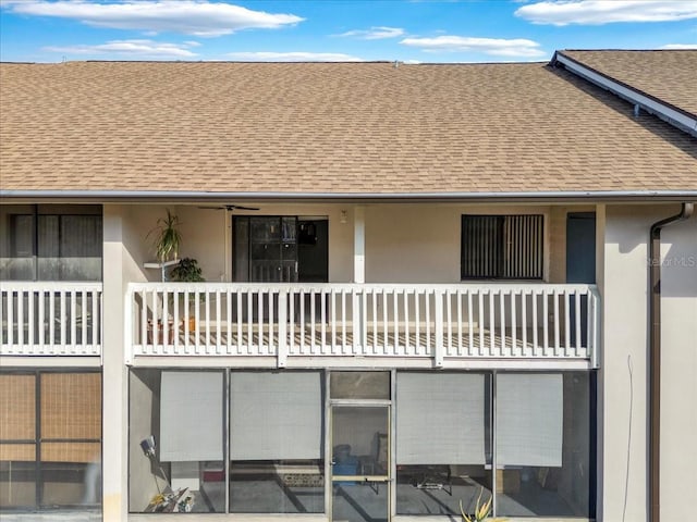 back of property with a shingled roof, a balcony, and stucco siding