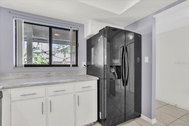 kitchen featuring light tile patterned floors, light countertops, white cabinetry, baseboards, and black fridge