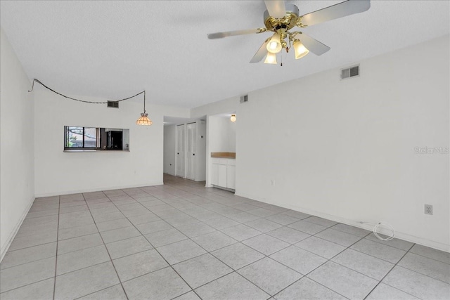 empty room with light tile patterned floors, a textured ceiling, visible vents, and a ceiling fan