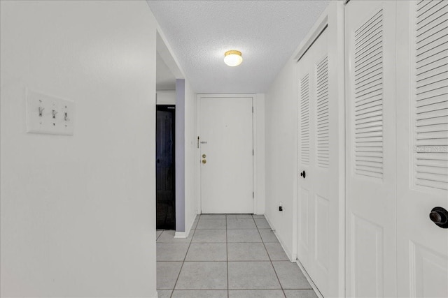 hall with light tile patterned flooring, a textured ceiling, and baseboards