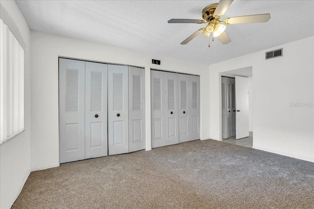 unfurnished bedroom featuring two closets, light colored carpet, visible vents, a ceiling fan, and a textured ceiling