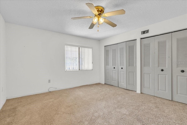 unfurnished bedroom with light carpet, visible vents, ceiling fan, a textured ceiling, and multiple closets