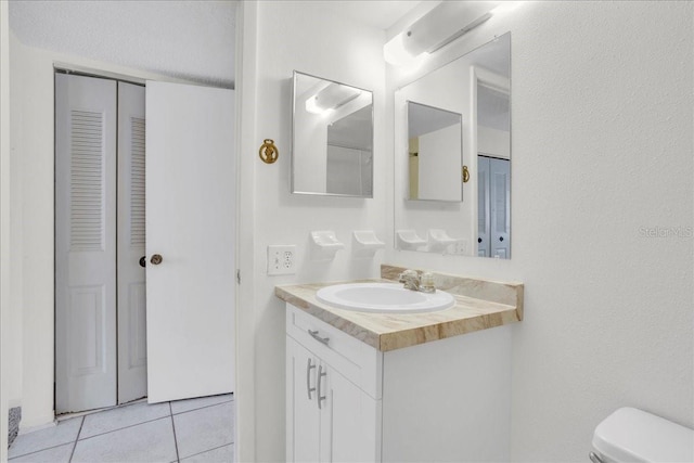 half bath featuring a closet, vanity, toilet, and tile patterned floors