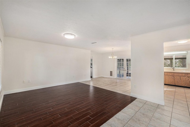 empty room featuring french doors, sink, an inviting chandelier, a textured ceiling, and light wood-type flooring