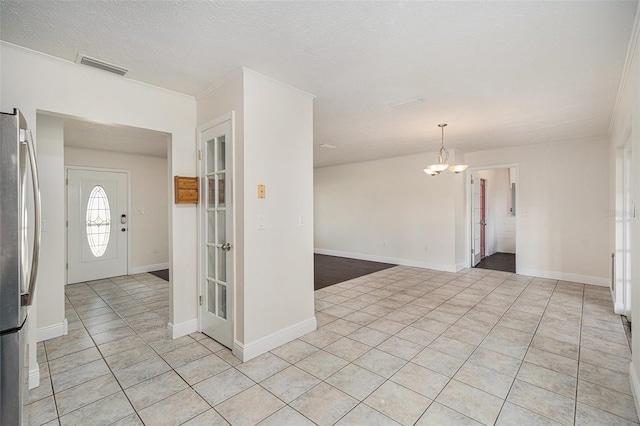 entryway with light tile patterned floors, ornamental molding, a textured ceiling, and an inviting chandelier