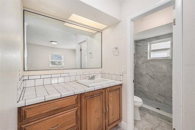 bathroom with a tile shower, tile patterned flooring, a textured ceiling, toilet, and vanity