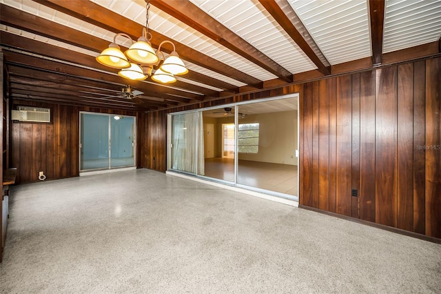 spare room featuring beamed ceiling, ceiling fan with notable chandelier, and wood walls