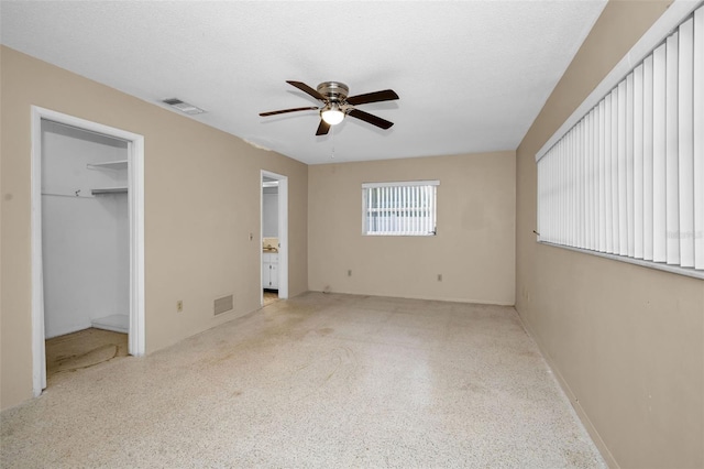 unfurnished bedroom featuring a textured ceiling, a walk in closet, a closet, and ceiling fan