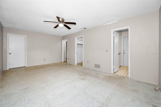 unfurnished bedroom featuring ceiling fan, ensuite bathroom, and a spacious closet