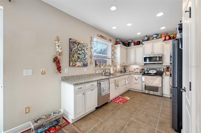 kitchen with white cabinets, stainless steel appliances, light stone counters, and sink