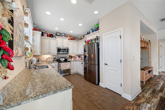 kitchen featuring light stone countertops, appliances with stainless steel finishes, dark tile patterned floors, sink, and white cabinets