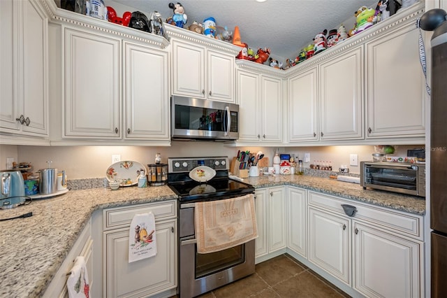 kitchen with a textured ceiling, stainless steel appliances, white cabinetry, and dark tile patterned floors