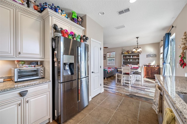 kitchen featuring light stone counters, pendant lighting, stainless steel refrigerator with ice dispenser, and an inviting chandelier