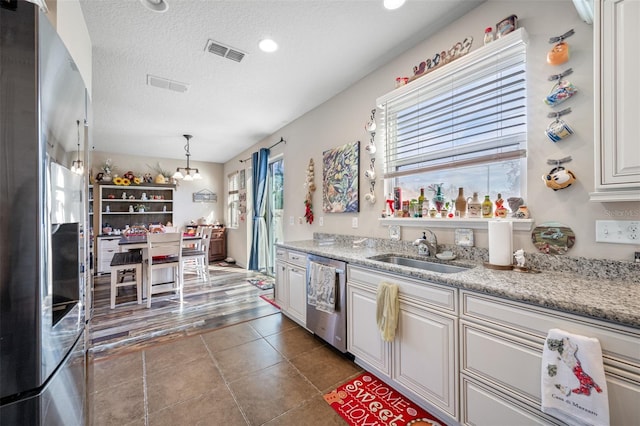 kitchen with white cabinetry, sink, stainless steel appliances, light stone counters, and decorative light fixtures