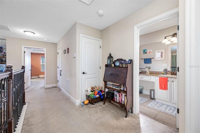 hallway with a textured ceiling and light carpet