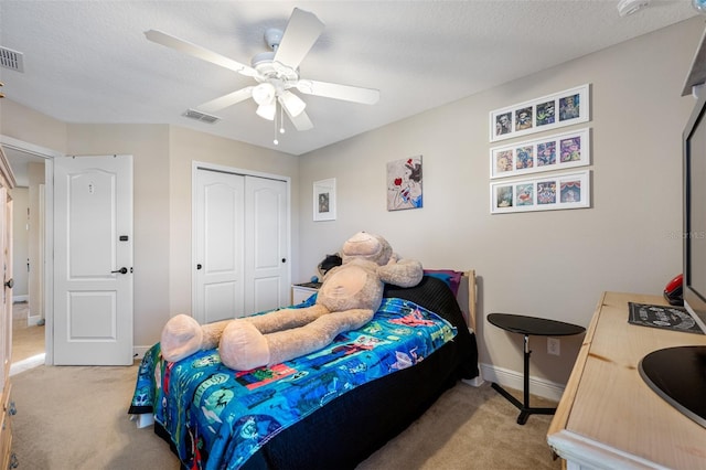 bedroom featuring ceiling fan, light colored carpet, a textured ceiling, and a closet