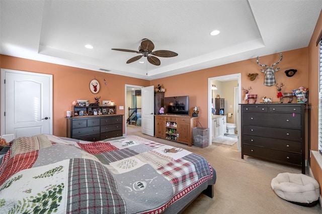 carpeted bedroom with a tray ceiling, ceiling fan, and ensuite bathroom