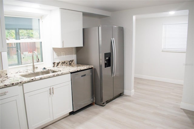 kitchen featuring appliances with stainless steel finishes, light wood-type flooring, light stone counters, sink, and white cabinetry