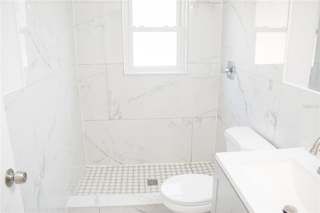 bathroom with a tile shower, vanity, tile walls, and toilet